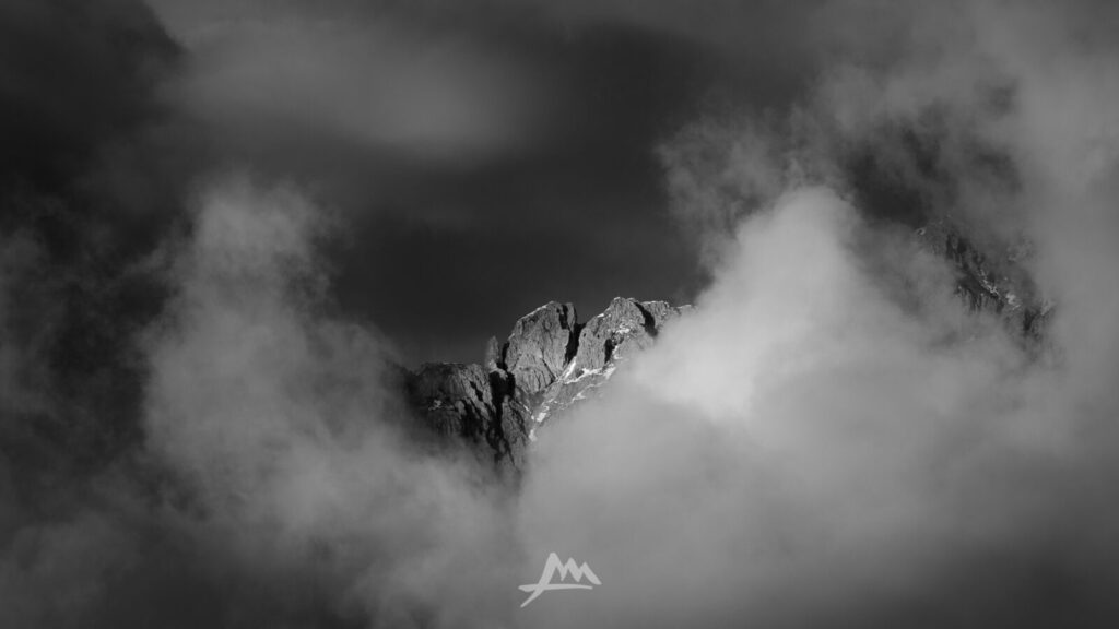 Una vetta avvolta dalla nebbia fitta, i contorni delle rocce sfumano nel bianco