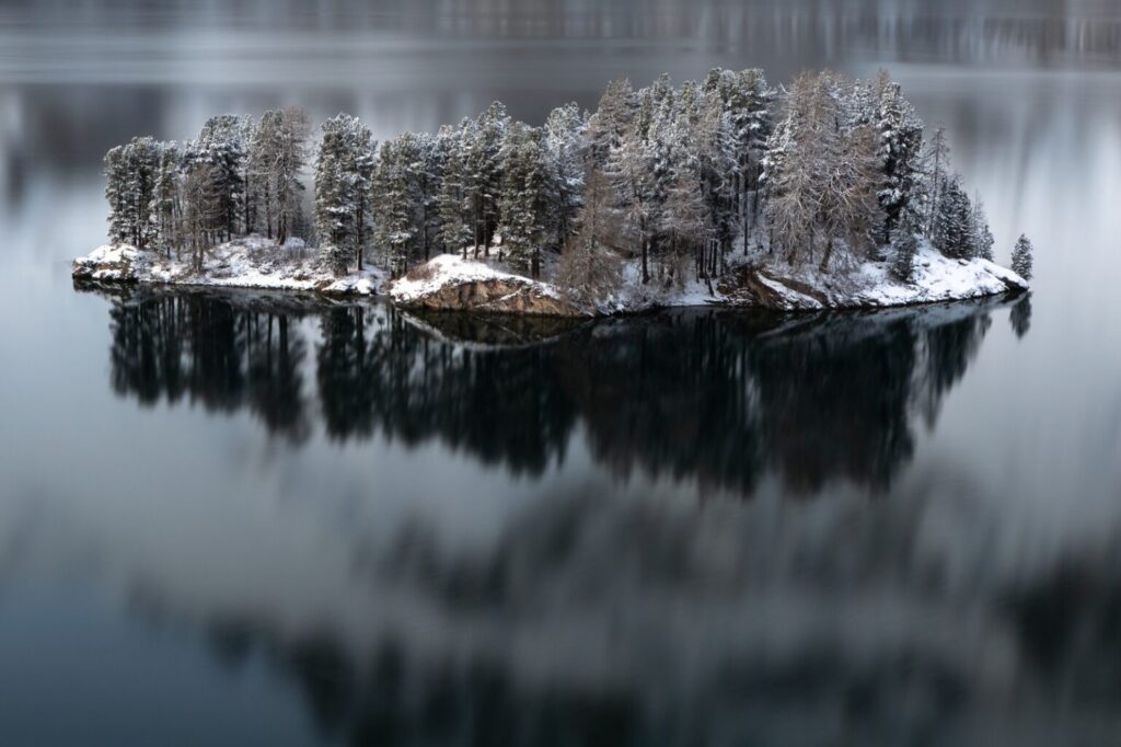 Lago di Sils in inverno con isola di Chaviolas riflessa sull'acqua ferma, Engadina
