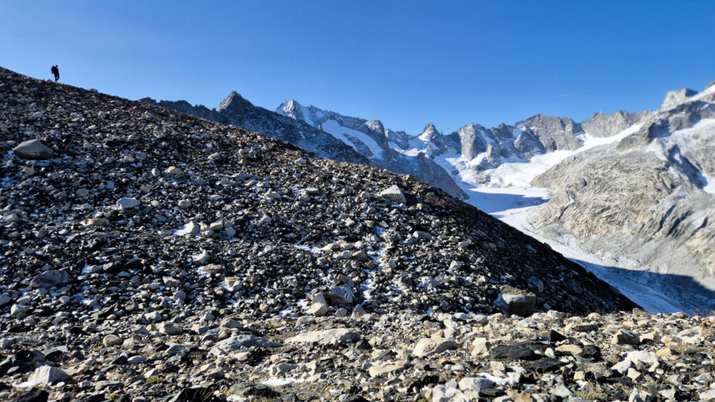 Figura isolata cammina tra rocce e neve in un altopiano d'alta quota