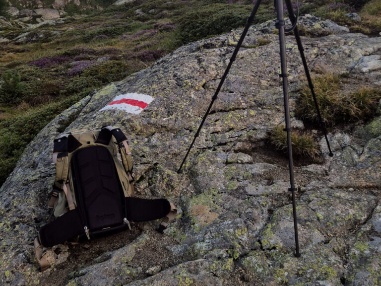 Zaino da montagna aperto sul sentiero all'alba, pronto per la scelta di cosa portare a valle.